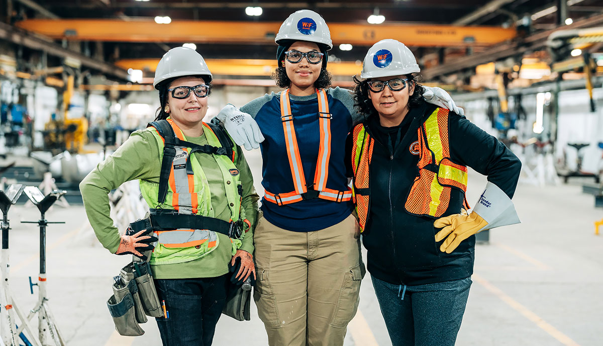 Three women in safety gear and work clothes at a work site