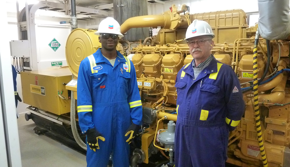 Two Chevron employees standing beside a dual fuel engine